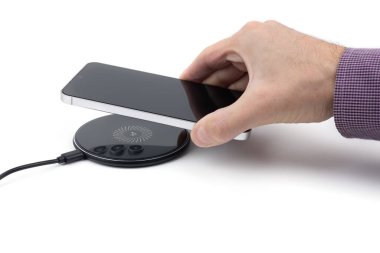 Masada kablosuz şarj cihazıyla cep telefonu bataryası şarj ediliyor. Akıllı telefon şarj cihazına yükleniyor. Kablosuz şarj cihazının yanındaki cep telefonu Modern yaşam tarzı teknolojisi