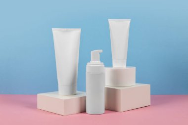 Reklamlar için güzel kozmetik şablonlar, plastik krem tüpleri ve podyumlu mavi arka planda şişeler. Premium ürün için güzellik tasarımı
