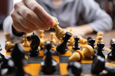 Masada otururken satranç tahtasının üzerindeki satranç taşını kapat. Oturma odasında abur cubur ve içeceklerle otururken arkadaşlarla strateji oyunu oynayan kişi.