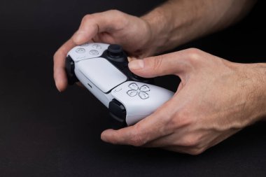 Dnipro Ukrayna - dec 29, 2024: Dualsense kontrol cihazını kullanarak bilgisayar oyunları oynamak. Playstation 5 denetleyicisi tutan adam.