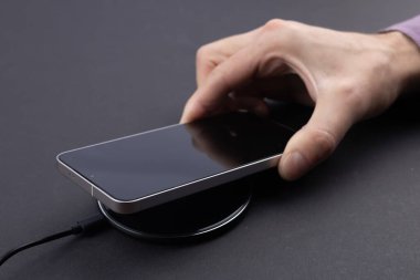 Masada kablosuz şarj cihazıyla cep telefonu bataryası şarj ediliyor. Akıllı telefon şarj cihazına yükleniyor. Kablosuz şarj cihazının yanındaki cep telefonu Modern yaşam tarzı teknolojisi