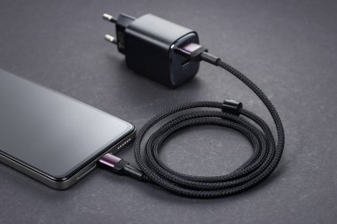 Gri arkaplanda AC şarj cihazı ve akıllı telefon..