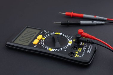 Digital multimeter with probes and display isolated on dark background. Electrical tool. Black digital multimeter with probes on a dark background, the multimeter is an electronic measuring instrument clipart