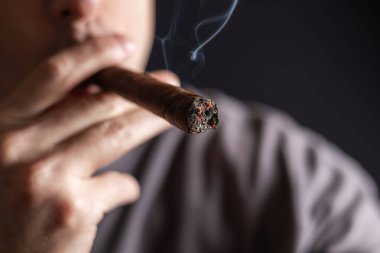 Bir adam siyah arka planda puro içiyor..