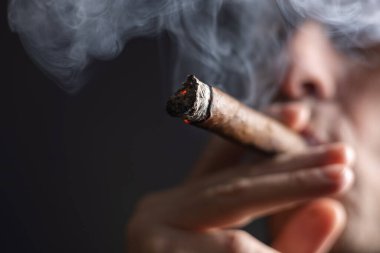 Bir adam siyah arka planda puro içiyor..