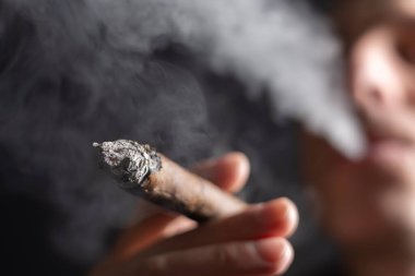 Bir adam siyah arka planda puro içiyor..