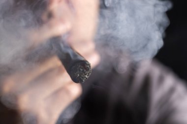 Bir adam siyah arka planda puro içiyor..