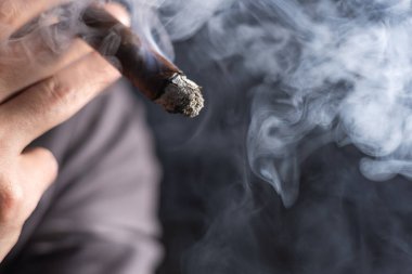 Bir adam siyah arka planda puro içiyor..