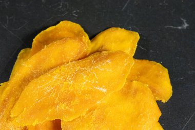 Koyu arkaplanda kurumuş mango dilimleri var..