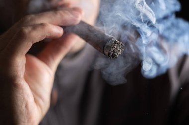 Bir adam siyah arka planda puro içiyor..