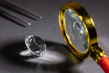 Büyüteç ve cımbızla karanlık bir zemin üzerinde parlak elmas.