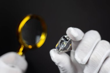 Erkek kuyumcu cilalanmış elması büyüteçle inceliyor. Alıcı elması kontrol ediyor. Kesilmiş ve cilalanmış elmas. Değerlendirme aşamasındaki elmas mücevherler. Loupe 'a bakan kuyumcu..