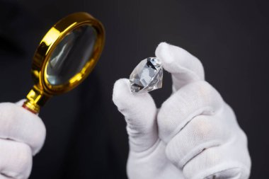 Mücevher aletleriyle cilalanmış elmasların değerlendirilmesinde elmas uzmanının ellerinin yakınlaştırılması.
