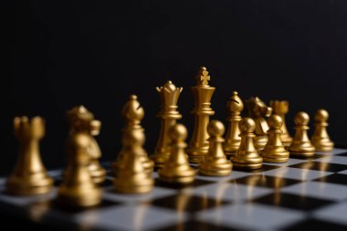 Altın satranç taşı elementi, kral, vezir kale, fil, at, satranç tahtasında duran piyon karanlık arka plan, liderlik, takım çalışması, ortaklık, iş stratejisi konsepti.