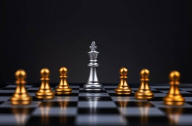 Lider, iş stratejisi ve planlama konsepti satranç tahtasındaki gümüş satranç kralı figürü ve rakip ya da düşmana karşı birkaç altın satranç piyonuyla çevrili. Çatışma, taktik, siyaset.