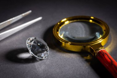 Büyüteç ve cımbızla karanlık bir zemin üzerinde parlak elmas.