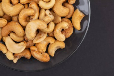 Koyu arkaplanda cam kasede kavrulmuş kaju fıstığı manzarası.