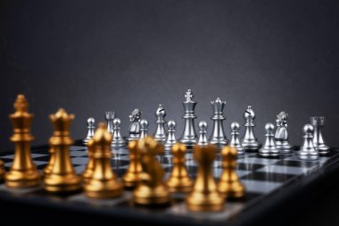 Tahta satranç tahtasına altın ve gümüş satranç figürleri yerleştirildi. İş hayatında entelektüel düello ve taktiksel savaş. Strateji planlaması, liderlik ve takım çalışması kavramı.