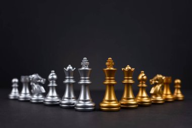 Altın ve gümüş satranç, Kral kraliçe at gemisi ve ticari savaş ve rekabet stratejisi konsepti için karanlık arka planda piyon içerir.