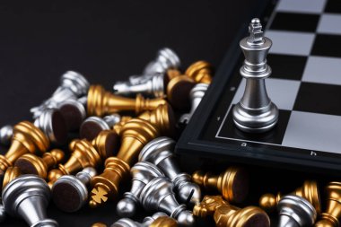 Gümüş papazın gümüş ve altın satranç taşlarıyla çevrili en iyi görüntüsü satranç tahtasının arkasında yatıyor. Karanlık arkaplanlı oyun yarışması, satranç savaşı, zafer, başarı, takım lideri