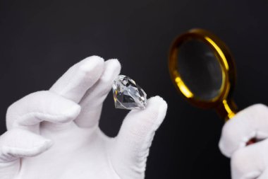 Erkek kuyumcu cilalanmış elması büyüteçle inceliyor. Alıcı elması kontrol ediyor. Kesilmiş ve cilalanmış elmas. Değerlendirme aşamasındaki elmas mücevherler. Loupe 'a bakan kuyumcu..
