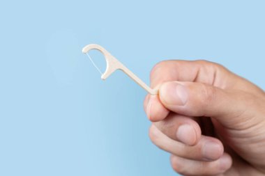 Mavi arka planda diş ipi tutan adam. Ağız ve diş bakımı.