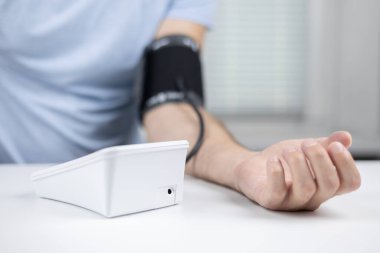 Eller masanın üzerinde bir tonometre ile. Gömlekli bir adam elektronik tonometreyle kan basıncını ölçer..