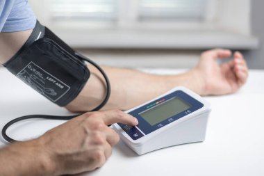 Eller masanın üzerinde bir tonometre ile. Gömlekli bir adam elektronik tonometreyle kan basıncını ölçer..