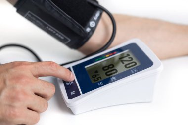 Eller masanın üzerinde bir tonometre ile. Gömlekli bir adam elektronik tonometreyle kan basıncını ölçer..
