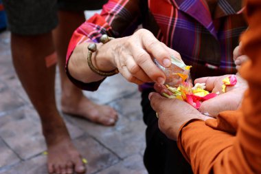 Songkran festivali sırasında, dindarlar Budist rahipler için geleneksel bir su dökme töreni düzenlemek için sıralarını sabırla beklerken uzun kuyruklar oluşuyor. Küçük kaseler kullanarak, çiçek kokulu suyu rahiplerin avuçlarına damga olarak dökerler.