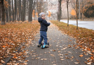 2 yaşındaki mutlu çocuk sonbaharda mobilete biniyor. Soğuk mevsimde açık hava oyunları.