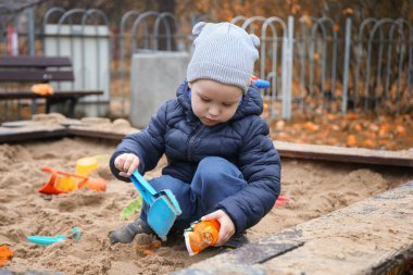 2 yaşındaki bir çocuk sonbaharda oyun bahçesinde oynar, mutlu bir çocuk kum havuzunda oynar. Soğuk sezon ve oyunlar