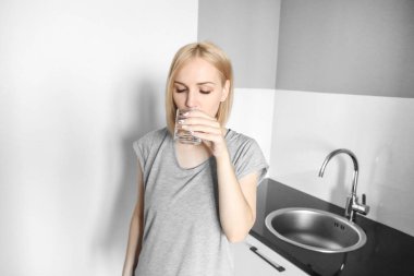 Sarışın kız mutfakta su içiyor. Sabahları bir bardak su. Antrenmandan sonra su iç.