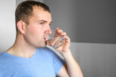 Bir adam mutfakta su içer. Sabahları bir bardak su. Antrenmandan sonra su iç.