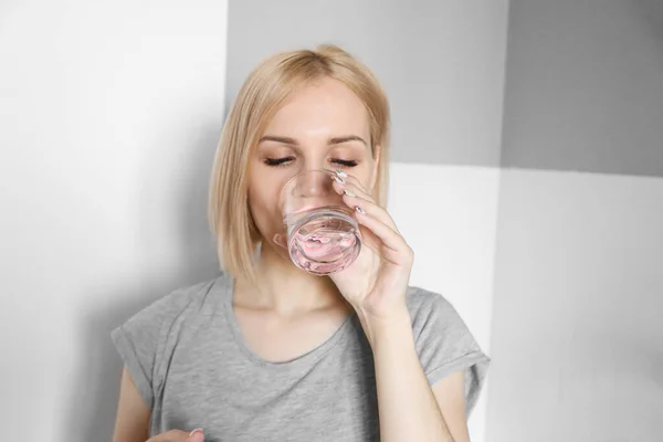 Blonde girl drinks water in the kitchen. Glass of water in the morning. Drink water after workout