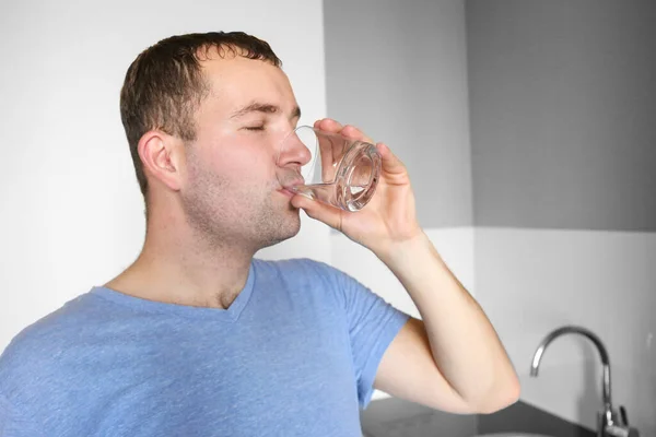 A man drinks water in the kitchen. Glass of water in the morning. Drink water after your workout