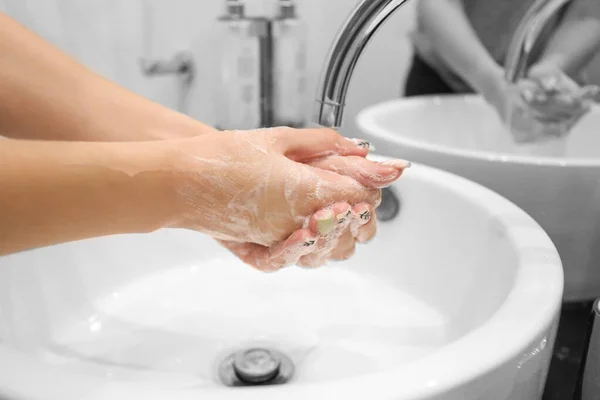 A woman is washing soap foam from her hands under running water. Hygiene. Washing hands in the bathroom