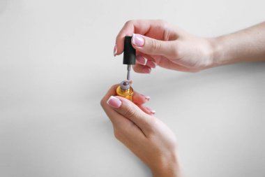 Güzel, uzun tırnaklı bir kız beyaz arka planda jöle ojesi tutuyor.