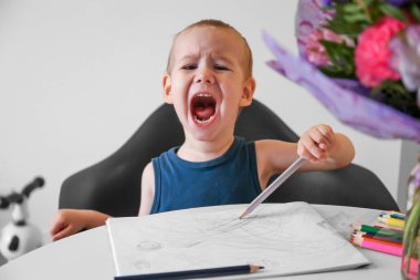 2 yaşındaki bir çocuk renkli kalemlerle bir albüm çiziyor ve çığlık atıyor. Kötü ruh hali. Bir çocuk tarafından çizim yoluyla duyguların ifadesi.