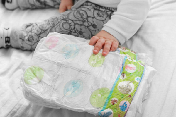 счастливый ребенок держит подгузник в руках. Закрывай. ребенок окружен памперсами на белом фоне