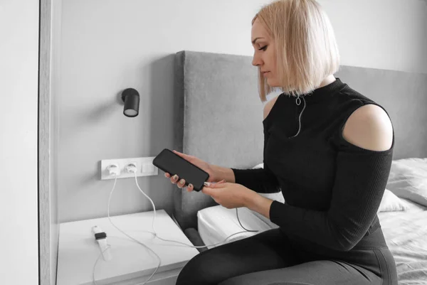blonde girl puts her devices on charge in the bedroom, smart watch, phone on charge on the bedside table