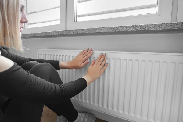 a woman sits near a heating radiator and checks the heat. Growth of utility bills. a crisis. Expensive heating bill