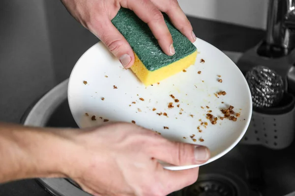 Man washes a plate after dried porridge in the sink. Help wife with housework.