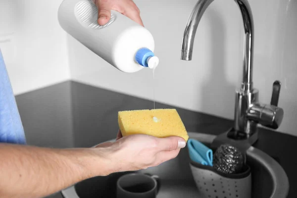 A man washes dishes in the sink, pours detergent on a sponge. Help your wife around the house.