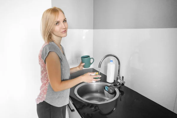 Happy blonde woman washes dishes and cups in the sink with her hands. Washing dishes by hand
