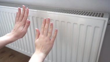 the girl touches the radiator with her hands. Turn off the heating, expensive heating. Increase in utility prices. Its cold in the house. High quality 4k footage