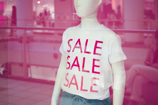 Discounts in the store. Children\'s mannequin with a discount t-shirt behind the glass of a shop in a mall