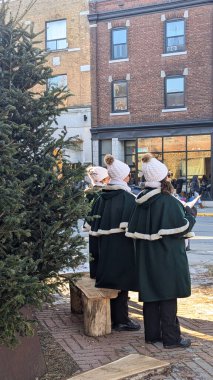 A group of Christmas Carole singers singing outdoors, dressed in green fur-trimmed coats and knit hats with pom-poms. Concept of Christmas, Carole, singer, winter fashion, songs. clipart