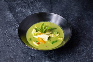 green soup with chicken and vegetables on a black background