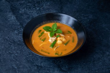 pumpkin soup with vegetables and herbs on a dark background.